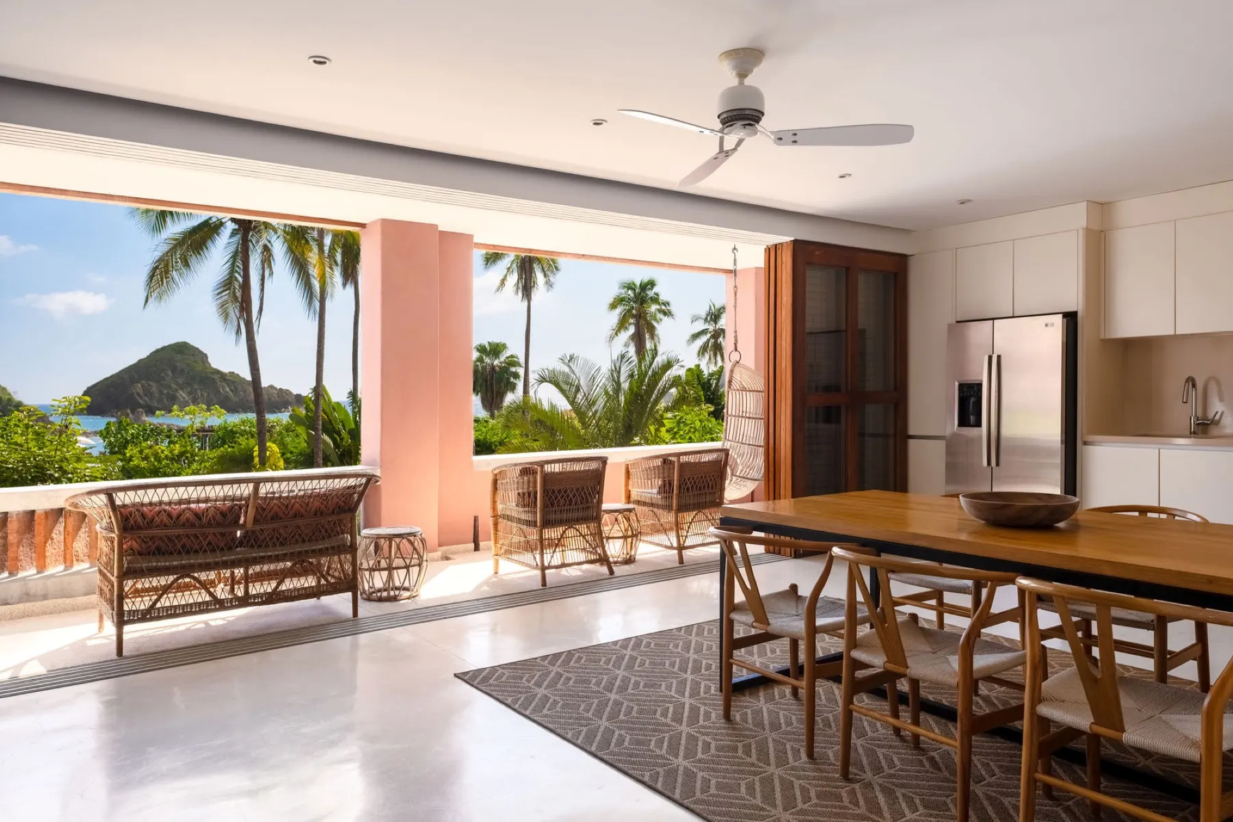Dining table and covered terrace with palms and a glimpse of the coast